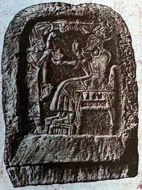 Steinrelief mit abgerundetem Rahmen: Links steht eine kleinere Gestalt und reicht etwas dar, rechts sitzt eine größere bärtige Gestalt auf einem Lehnstuhl mit hoher Kopfbedeckung.