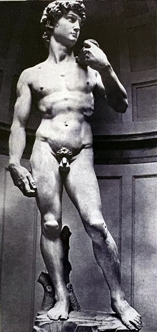 Schwarzweißfoto einer Marmorstatue: ein nackter junger Mann mit lockigem Haar, stehend, das Gewicht auf dem rechten Bein, die linke Hand an der Schulter, den Kopf zur Seite gewandt.