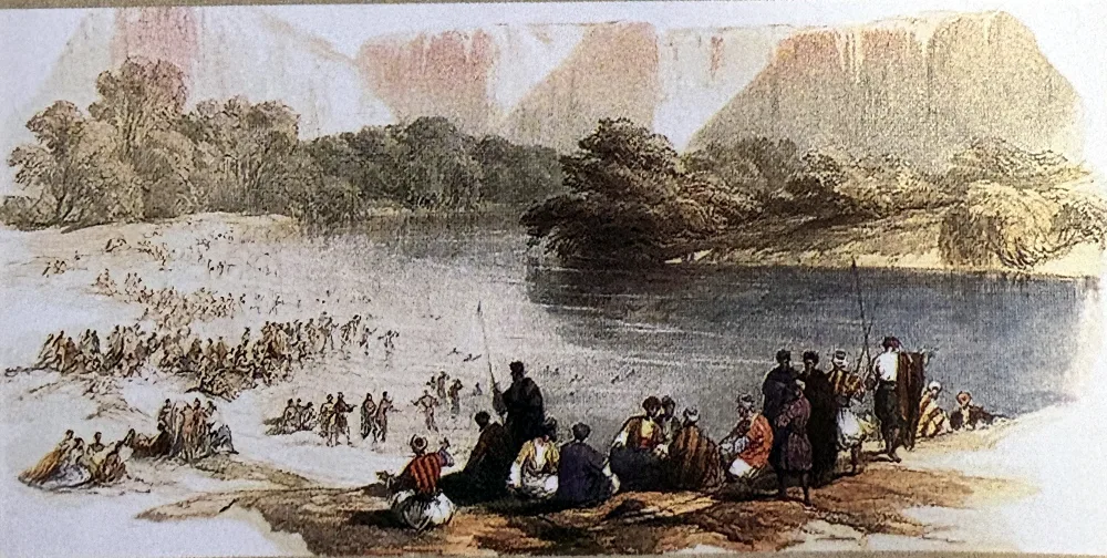Farbige Lithografie: Ein breiter Fluss zwischen Bäumen vor hohen, rötlichen Felswänden; links waten viele kleine Gestalten durch das Wasser, vorn sitzt und steht eine Gruppe von Menschen in bunten orientalischen Gewändern am Ufer.