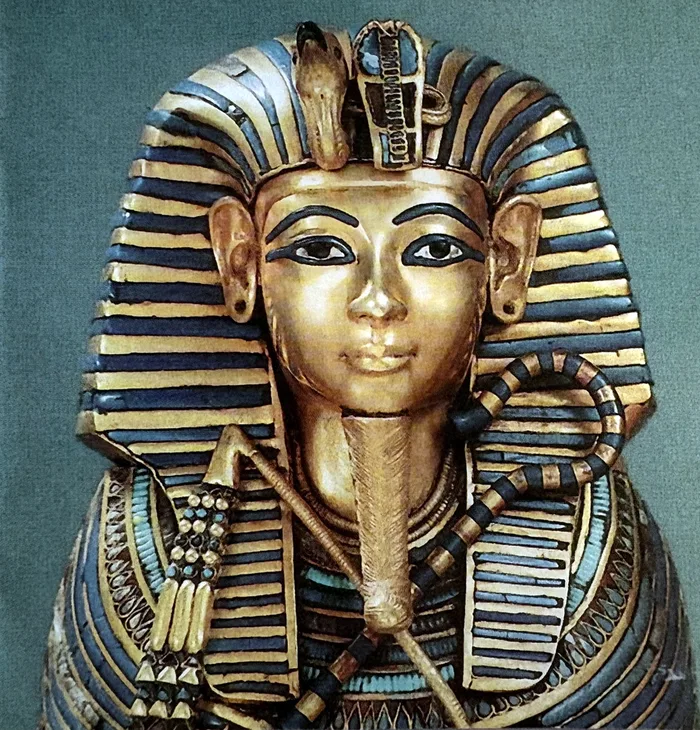 Farbfoto der goldenen Totenmaske des Tutanchamun vor grünem Hintergrund: ein Gesicht aus Gold mit dunkel umrandeten Augen, blau-golden gestreiftem Kopftuch, Geier- und Schlangenkopf an der Stirn, geflochtenem Kinnbart und breitem Halskragen.